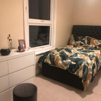 Bed with high headboard in dark brown and colourful duvet cover and white chest of draws