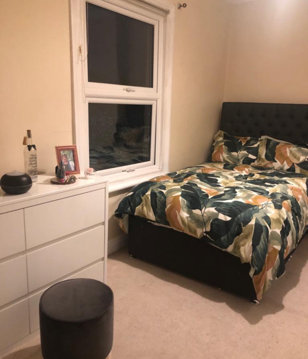 Bed with high headboard in dark brown and colourful duvet cover and white chest of draws
